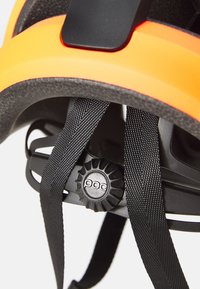 Leuchtend orange Fahrradhelm mit strukturiertem schwarzen Innenfutter, ausgestattet mit verstellbaren schwarzen Riemen und einem Drehregler zur Größenanpassung.