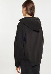 Felpa nera con texture a costine, vestibilità oversize e cappuccio con cordoncino. Presenta maniche larghe e un colore uniforme senza motivi.