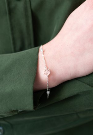 Silver bracelet featuring a spider web charm and small beads, worn on a wrist, against a green fabric background.