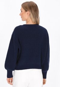 Marineblauwe gebreide trui met een gestructureerde afwerking en omgeslagen mouwen, voorzien van decoratieve knopen op de schouder en een cropped pasvorm.