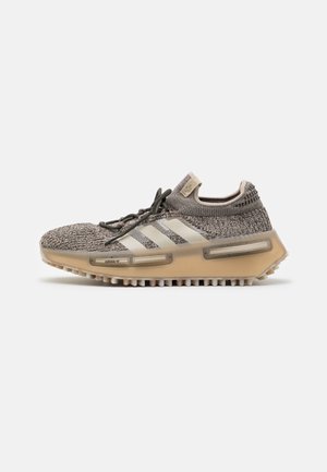 Grijze gebreide sneaker met witte accentstrepen, ronde neus en een dikke, doorschijnende zool met een gestructureerd profiel voor grip.