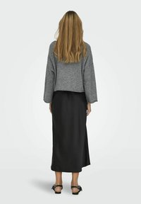 Grauer, cropped Pullover mit weiten Ärmeln, kombiniert mit einem schwarzen Satin-Maxirock mit einem Seitenschlitz und schwarzen, geschnürten Sandalen.
