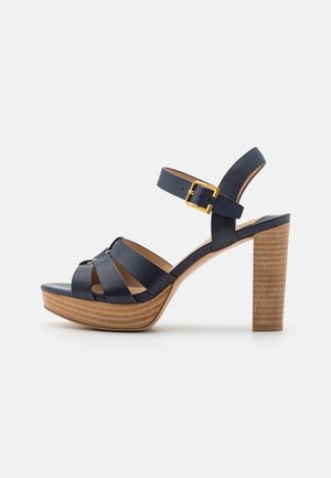 Navy blue high-heeled sandal with wooden platform and block heel, featuring an ankle strap with a gold buckle.
