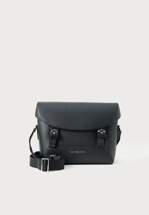 Borsa a tracolla nera in pelle con chiusura a patta, tracolla in tessuto regolabile, fibbie metalliche e logo Tommy Hilfiger sul pannello frontale.