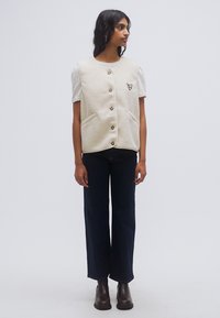 Μπεζ γιλέκο από φλις με τέσσερα κουμπιά, δύο μπροστινές τσέπες και μια μικρή κεντημένη λεπτομέρεια. Συνδυάζεται με σκούρο τζιν παντελόνι και καφέ μποτάκια στον αστράγαλο.