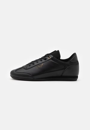 Black leather sneaker featuring a sleek design, round toe, gold eyelets, textured side accents, and a padded collar for comfort.