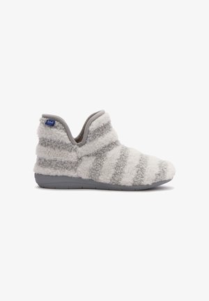 Zapatilla de rayas blancas y grises con una textura suave y peluda, diseño bajo en el tobillo, y una suela de goma gris para mayor agarre. Presenta una etiqueta de la marca en el lado.