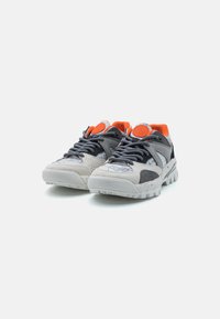 Baskets grises et blanches avec des accents orange, présentant un mélange de textures, y compris des surfaces lisses et en daim, ainsi qu'une semelle extérieure robuste.