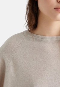 Felpa in lana beige con scollatura a girocollo, polsini a coste e una finitura morbida e testurizzata, che enfatizza un taglio morbido e un design casual.