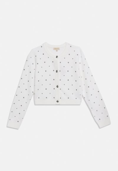 Λευκή κοντή ζακέτα με μακριά μανίκια, στρογγυλή λαιμό κοψη, μαύρα κυκλικά διακοσμητικά και τέσσερα κουμπιά στο κέντρο μπροστά.