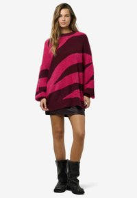 Fuzzy džemperis bordo krāsā ar rozā zigzaga rakstiem, plašām piedurknēm, kombinēts ar melnu ādas svārku un melniem zābakiem līdz ceļiem.