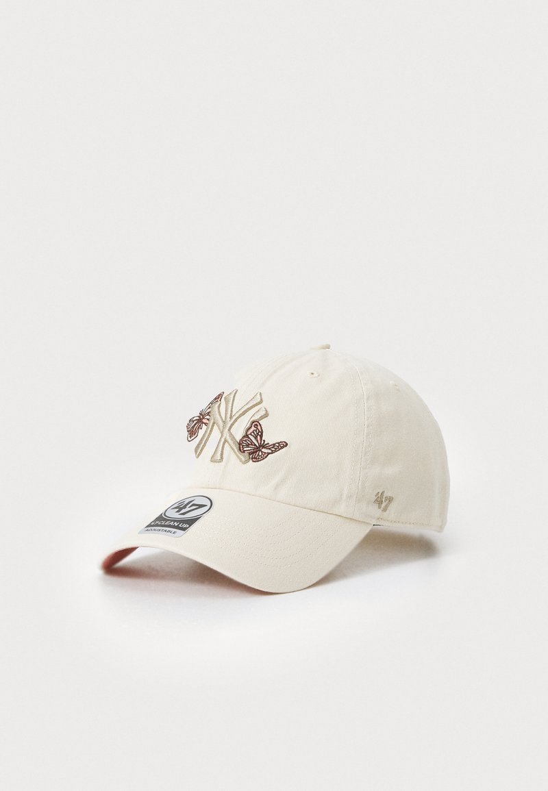 Krämmfärgad keps med broderad "NY"-logotyp och fjärilsdetaljer, med en böjd skärm och justerbart band bak.