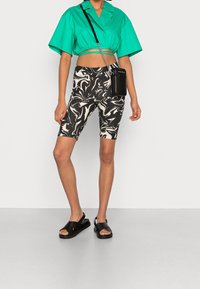 Chemise turquoise courte, cuissards marbrés noir et blanc, et sandales noires à lanières croisées. Comprend un petit sac bandoulière noir.