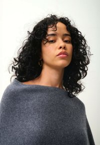 Sciarpa di lana grigia con una caduta morbida, texture liscia e scollatura ampia, indossata da un modello. Capelli ricci incorniciano il viso.