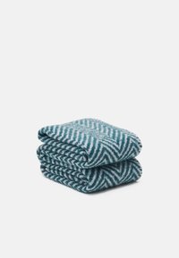 Deux couvertures pliées avec un motif chevron en bleu sarcelle et blanc. Fabriquées en tissu doux avec une finition texturée.