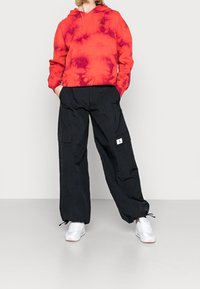 Rød tie-dye hoodie med en frontlomme og snore, parret med sorte cargo-bukser med sidelommer og hvidt logo-plaster.