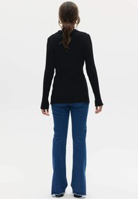 Czarny prążkowany top z długim rękawem o dopasowanym kroju, w połączeniu z niebieskimi dżinsami w stylu dzwonów z postrzępionymi brzegami. Prosty i funkcjonalny design.
