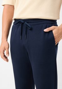Tmavě modré joggingové kalhoty vyrobené z měkké tkaniny, s elastickým pasem se šňůrkami a bočními kapsami, předvádějící texturovaný povrch.