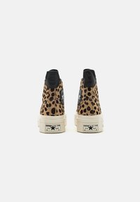 Aukštos sportinės kedai iš smėlio spalvos dirbtinės kailio su juodais leopardo taškais, juodomis odos detalėmis ir baltais guminiais padais, turinčiais "Converse All Star" ženklinimą.