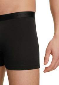 Boxer neri realizzati in tessuto morbido con una cintura elastica soffice, caratterizzata da lettering in rilievo. Immagine ravvicinata che mostra il dettaglio laterale dei pantaloni.