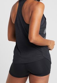 Czarny sportowy top bez rękawów z designem typu racerback i lekko zakrzywionym dołem. Połączony z czarnymi szortami, prezentującymi gładką fakturę.