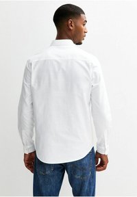 Camicia bianca a maniche lunghe realizzata in tessuto leggero, con colletto alla francese e polsini con un bottone, abbinata a jeans blu in denim.