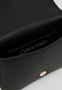 Sort læderhåndtaske med tekstureret finish, med en guldtryklås og et mærket interiøretiket. Glat, struktureret design.