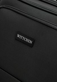 Borsa da viaggio nera con tessuto testurizzato, multiple cerniere e una toppa loggata rettangolare che mostra il marchio "WITTCHEN."