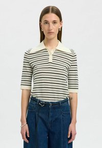 Krämfärgad och svartrandig polo skjorta med spetsig krage och korta �ärmar, tillsammans med löst sittande blå denimbyxor med dragsko.