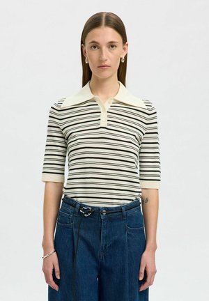 Krämfärgad och svartrandig polo skjorta med spetsig krage och korta ärmar, tillsammans med löst sittande blå denimbyxor med dragsko.