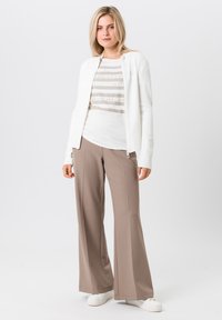 White zip-up jacket with textured sleeves, layered over a beige-striped T-shirt, paired with beige wide-leg pants and white sneakers.