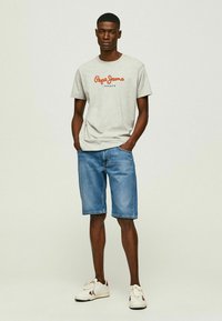 Pilkas medvilnės marškinėliai su raudonu "Pepe Jeans London" logotipu, derinami su mėlynomis džinsinėmis šortais. Balti sportbačiai su raudonais ir mėlynais akcentais.