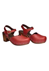 Sabots en cuir rouge à bout fermé avec des brides à la cheville, talons blocs en bois et clous décoratifs argentés le long des bords de la semelle.