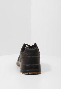 Schwarzer Sportschuh mit einem glatten Lederoberteil, gepolstertem Schaft, Schnürdesign und einer strukturierten Gummisohle.