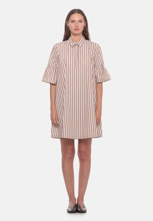 Donna che indossa un vestito beige e bianco a righe verticali fino al ginocchio con maniche corte arricciate e scarpe basse nere, in piedi rivolta in avanti.