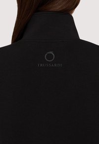 Černá mikina s vysokým límcem; na zadní straně s tonalním logem "TRUSSARDI" a emblémem. Hladká textura, ležérní design.
