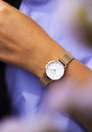 Reloj de esfera redonda con un dial blanco y acentos en oro rosa, que cuenta con una correa de malla de metal y marcadores horarios simples.
