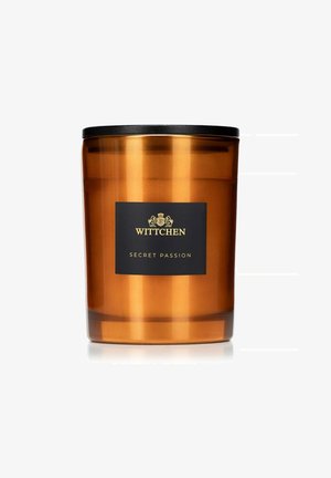 Bocal en verre ambre pour bougie avec un couvercle noir mat. Présente une étiquette noire avec du texte doré, indiquant "WITTCHEN SECRET PASSION."