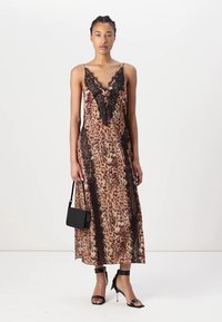 Abito midi con stampa leopardata, orlo in pizzo, spalline sottili, dettagli neri e un design fluente. La modella tiene in mano una piccola borsa nera.
