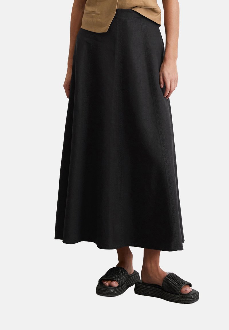 Jupe maxi noire avec une texture lisse et de subtiles coutures verticales ; associée à des sandales tissées noires avec une semelle plateforme.