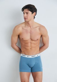Boxers de color azul claro, hechos de una tela suave, con una cinturilla blanca que lleva el logo negro de Nike, ajuste ceñido y longitud a mitad del muslo.