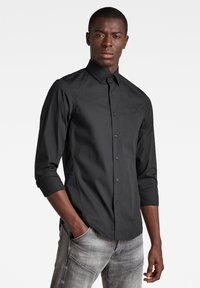 Camicia nera a maniche lunghe con colletto classico e un sottile dettaglio del logo sul petto, realizzata in tessuto liscio.