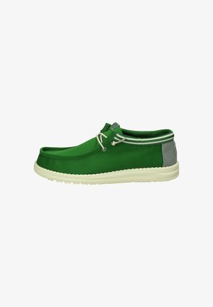 Scarpa slip-on verde in tela con accento grigio chiaro sul tallone, caratterizzata da una suola in gomma bianca e due dettagli decorativi a forma di lacci.