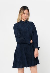 Navy blue dress with a buttoned collar, long sleeves, intricate floral embroidery, and a flared skirt with a textured fabric finish.