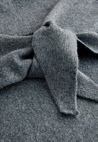 Grå tekstureret stof med en strikket fremtoning, der har en bundet knude detalje i forgrunden og en blød, fuzzy overflade.