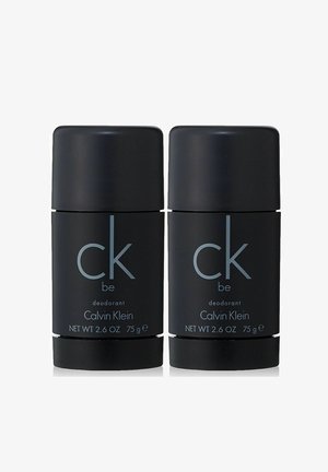 Kaksi mustaa sylinterimäistä deodoranttitikkuja, jotka on merkitty "CK Be" hopeateksteillä, 75 g (2,6 oz) kukin, ja joissa on sileä mattapintainen viimeistely.