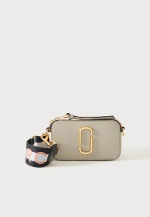 Sac bandoulière rectangulaire beige aux bords arrondis avec un logo double maillon doré, comprenant une sangle noire amovible avec lettrage rose et blanc.