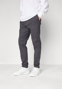 Pantaloni grigi, con texture, dal taglio affusolato, dotati di tasche laterali e una vita. Abbinati a sneakers bianche.