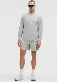 Lichtgrijze sportoutfit met een rits lange mouw top en bijpassende shorts. Gemaakt van een gladde stof, aangevuld met sportieve zonnebril.