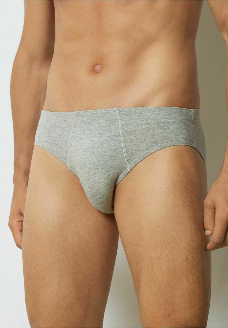 Grå bomullsunderkläder med en jämn textur, som har en låg midja, minimala sömdetaljer och en åtsittande passform mot en neutral bakgrund.